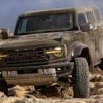 A green 2024 Ford Bronco for sale is shown driving off-road through a deser.