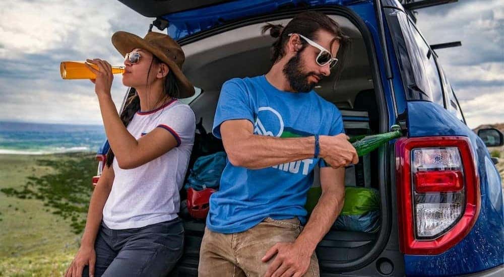 A blue 2024 Ford Bronco Sport is shown parked near two people drinking sodas.