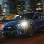 A blue 2024 Ford Mustang Mach-E GT is driving on a highway at night.