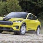 A yellow 2024 Ford Mustang Mach-E Rally Edition is shown kicking up dust off-road.