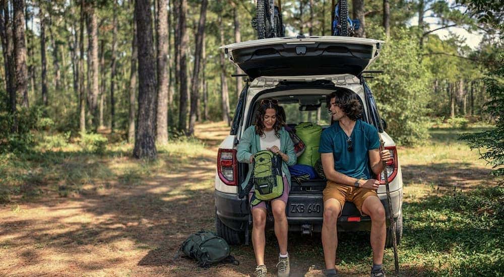 A man and a woman are sitting on the rear bumper of a white 2024 Ford Bronco Sport.