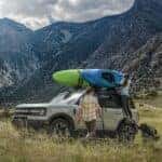 A grey 2024 Ford Bronco Sport is parked near a river with kayaks on the roof.