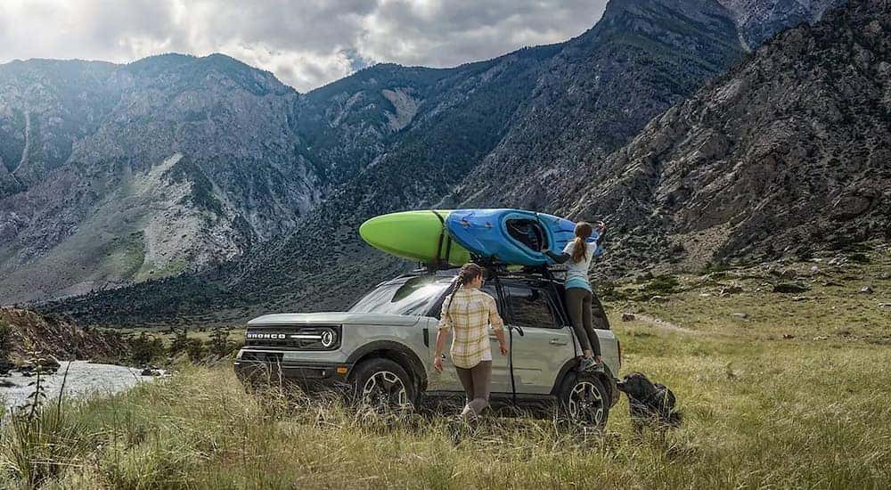 A grey 2024 Ford Bronco Sport is parked near a river with kayaks on the roof.
