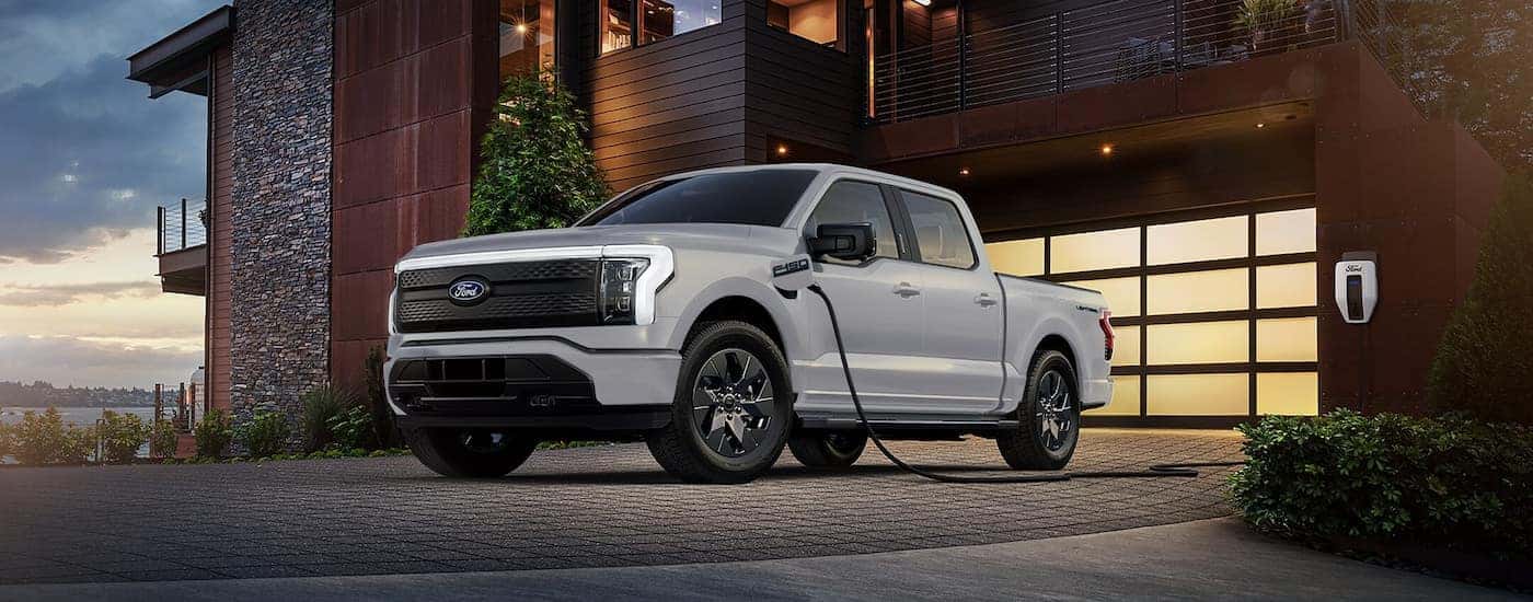 A white 2024 Ford F-150 Lightning plugged into a residential charger near a Ford dealer near Lebanon.