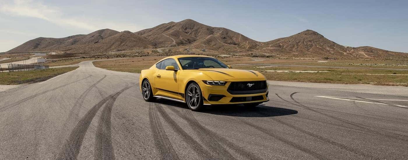 A yellow 2024 Ford Mustang parked on an empty track.