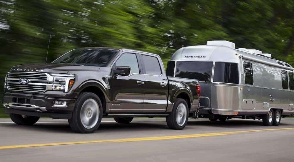 A black 2024 Ford F-150 Platinum is shown towing a trailer on a highway.
