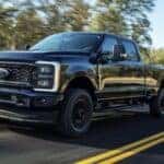 A black 2023 Ford F-250 XL is shown driving on a highway after viewing trucks for sale.