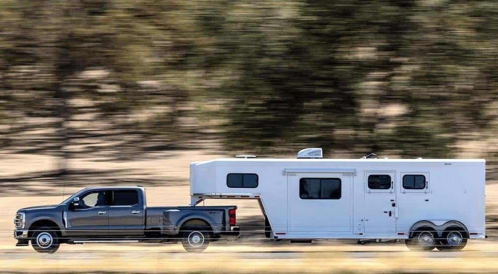 A gray 2024 Ford F-350 Lariat is shown towing a trailer on a highway.
