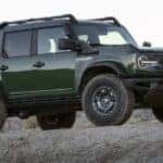 A green 2022 Ford Bronco Everglades is shown near a dealer with cars for sale.