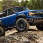 A blue 2025 Ford Bronco Raptor with Black Appearance Package off-roading over boulders.