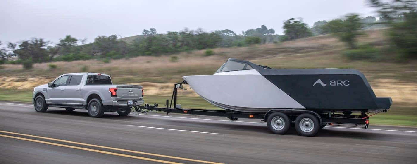 A silver 2024 Ford F-150 Lightning XLT is shown from the side while towing a boat.