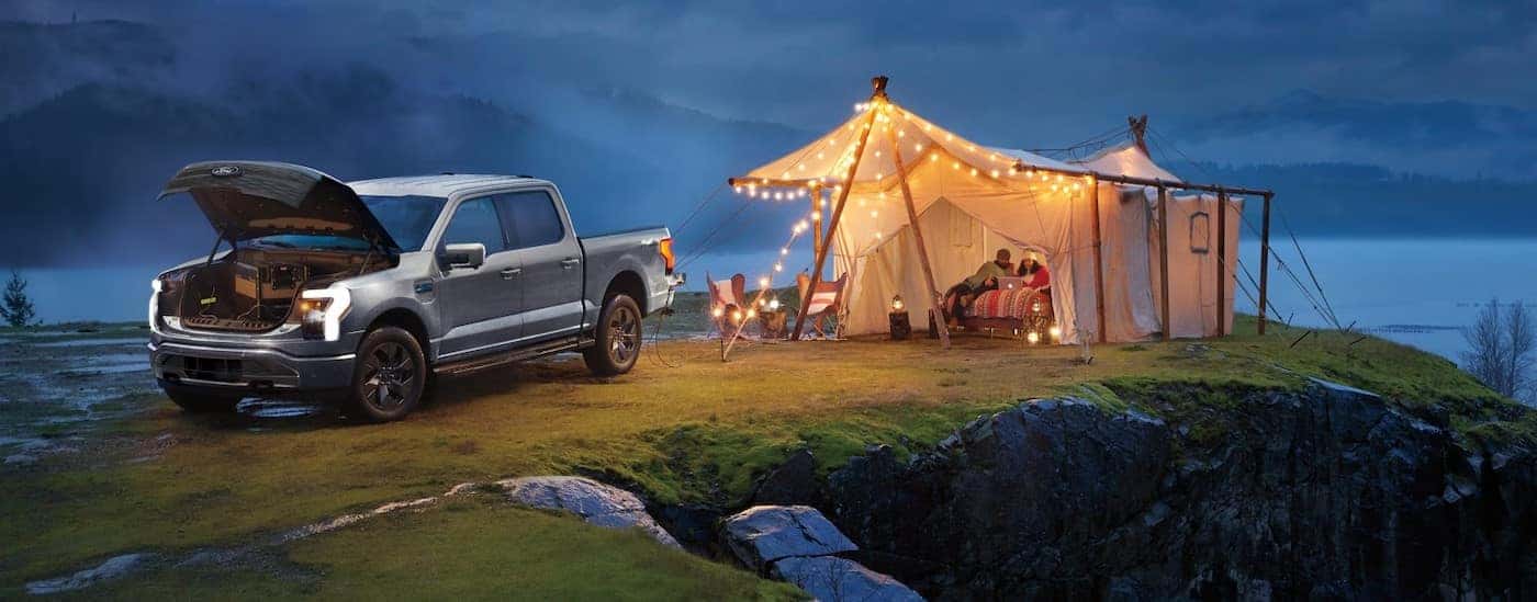 A silver 2025 Ford F-150 Lightning is shown parked near a well lit tent.