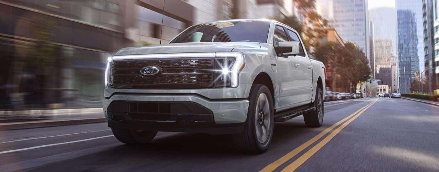 A white 2024 Ford F-150 Lightning for sale driving through a city.