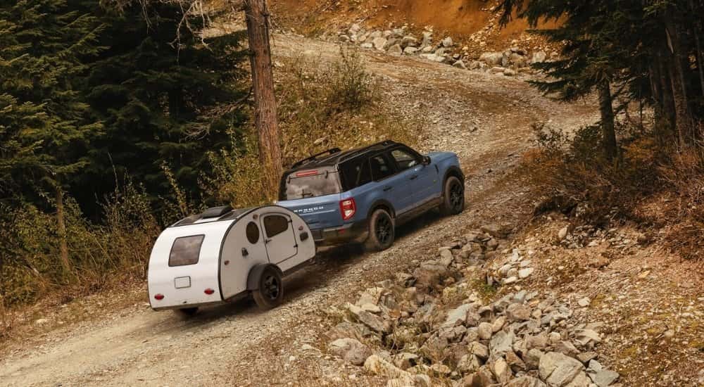 A blue 2025 Ford Bronco Sport Badlands is towing a trailer on a trail.