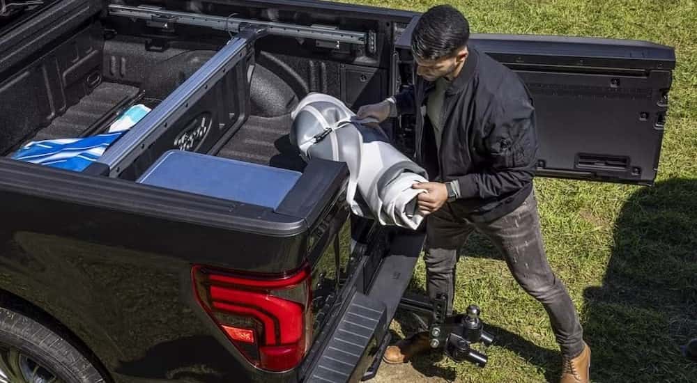Close-up of a person loading gear into the bed of a black 2025 Ford F-150.