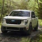 A white 2025 Ford Maverick for sale driving in a forest.