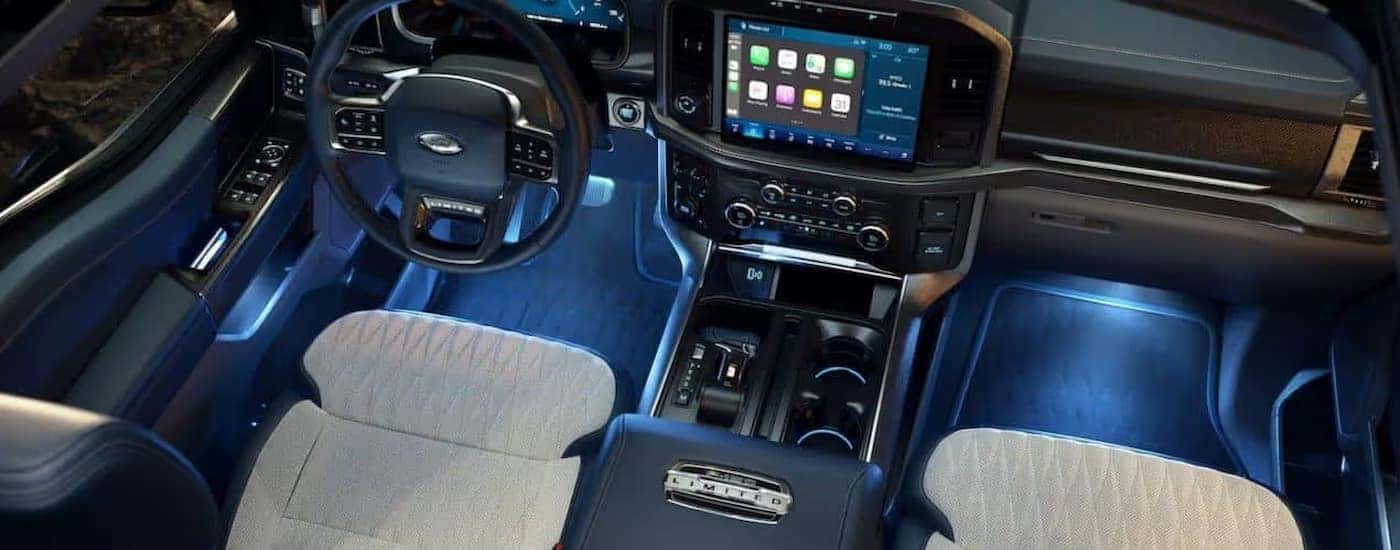 The blue-lit interior of a 2021 Ford F-150 Limited shows the steering wheel and infotainment screen.