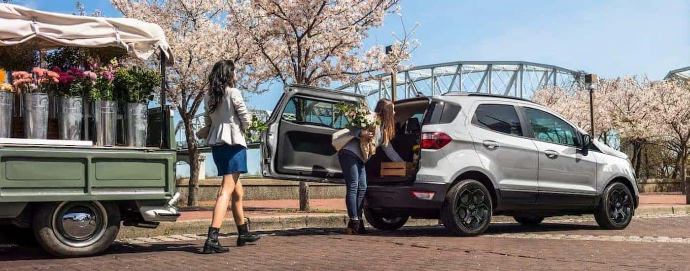 Two people loading flowers into the cargo area of a silver 2022 Ford EcoSport.