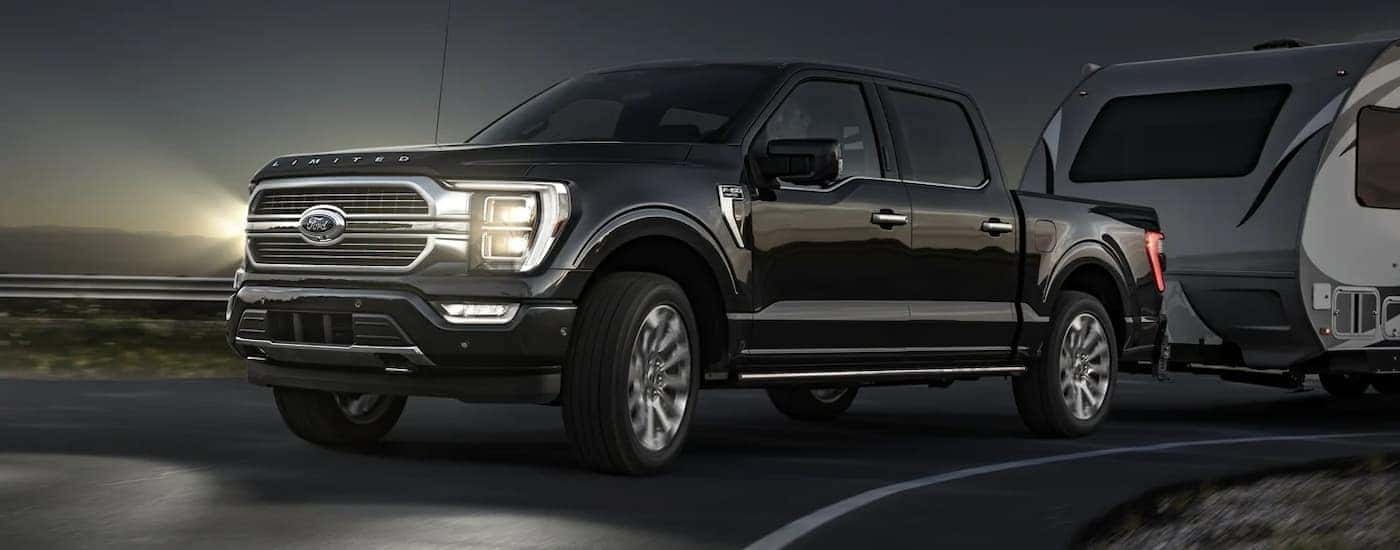 A black 2022 Ford F-150 Limited is shown towing a trailer at night.