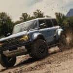 A blue 2025 Ford Bronco Raptor kicking up mud
