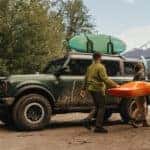 People carrying a kayak near a green 2025 Ford Bronco for sale near Indianapolis.