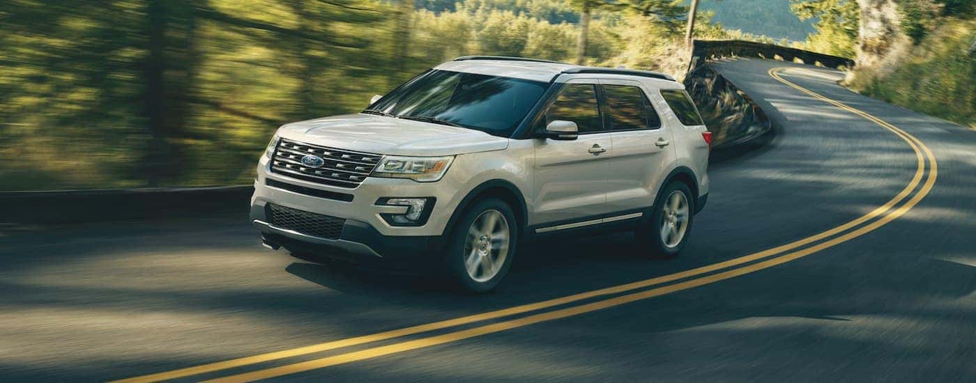 A white 2018 Ford Explorer is shown driving on a wooded road.