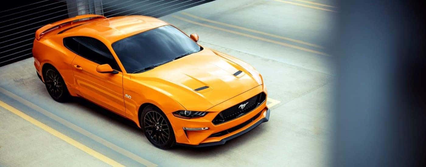 An orange 2018 Ford Mustang GT is shown parked on a parking garage.