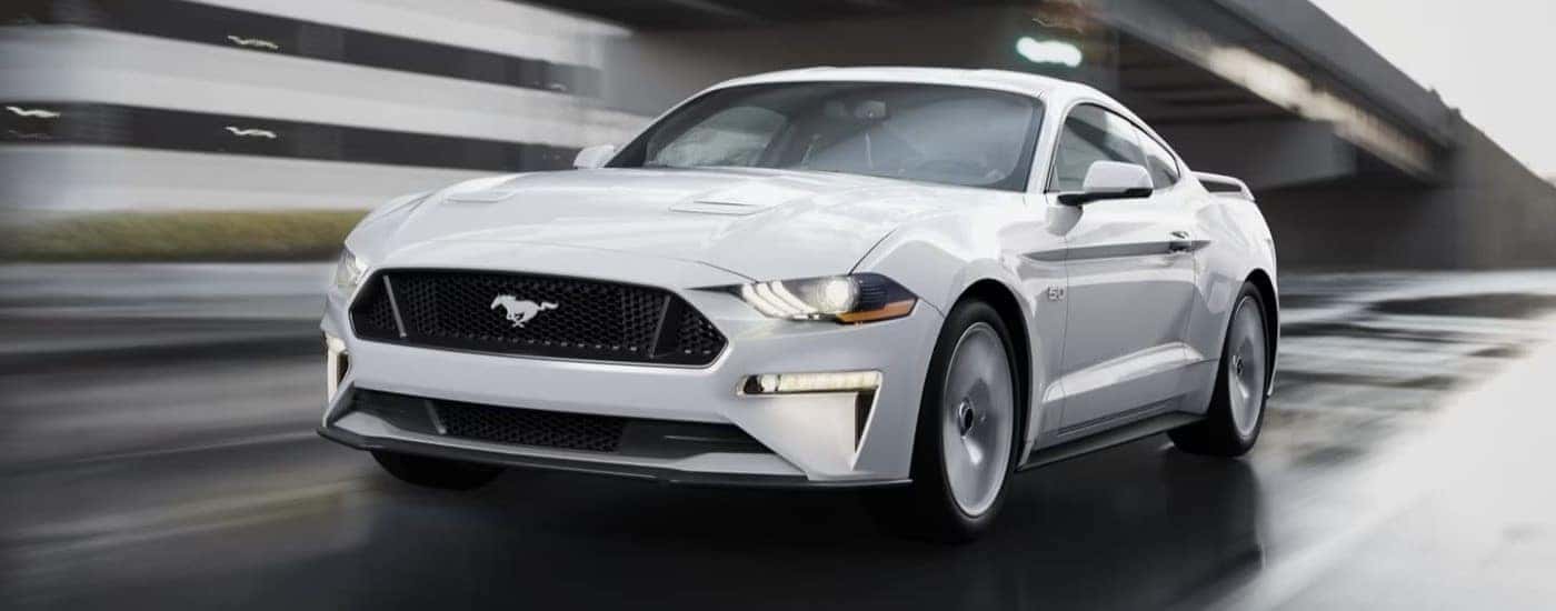 A white 2022 Ford Mustang GT is shown driving on a city street after leaving a used car dealer near Indianapolis.