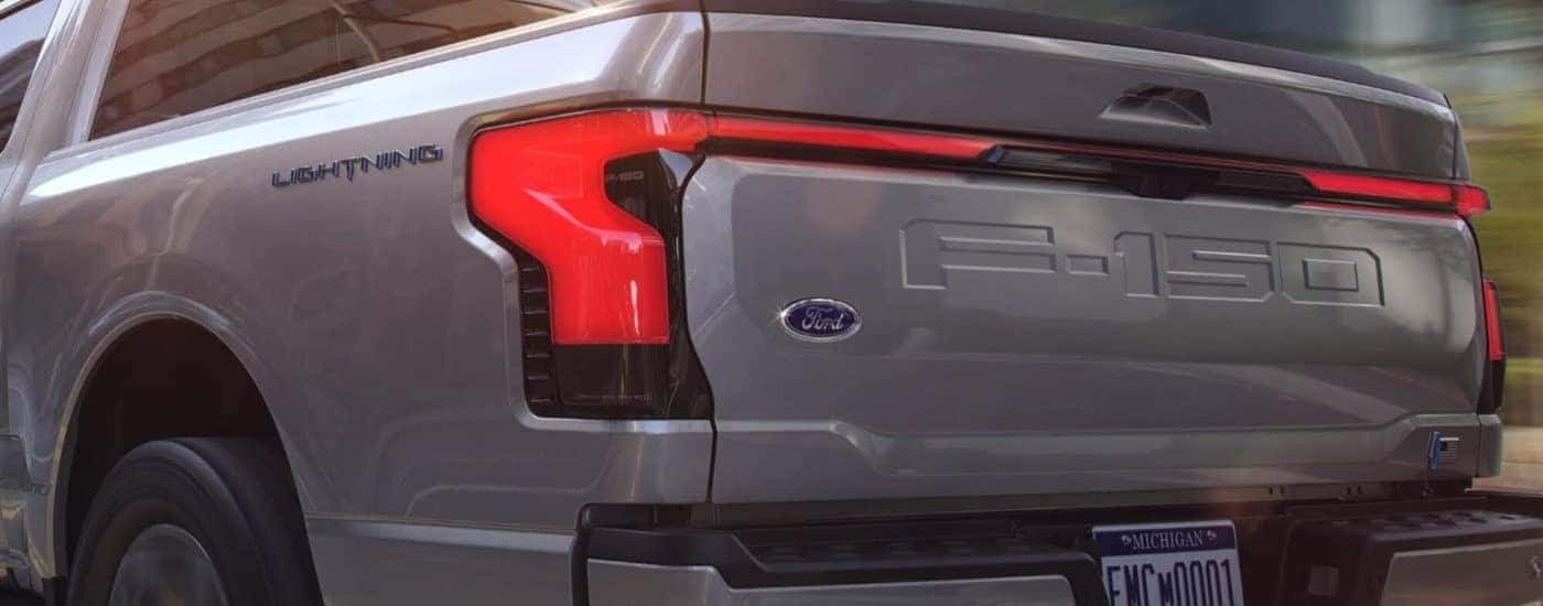 A silver 2024 Ford F-150 Lightning for sale is shown from the rear at an angle.