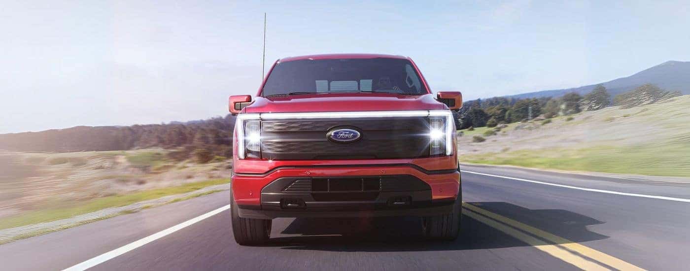 A red 2025 Ford F-150 Lightning for sale in Zionsville is shown driving on a highway