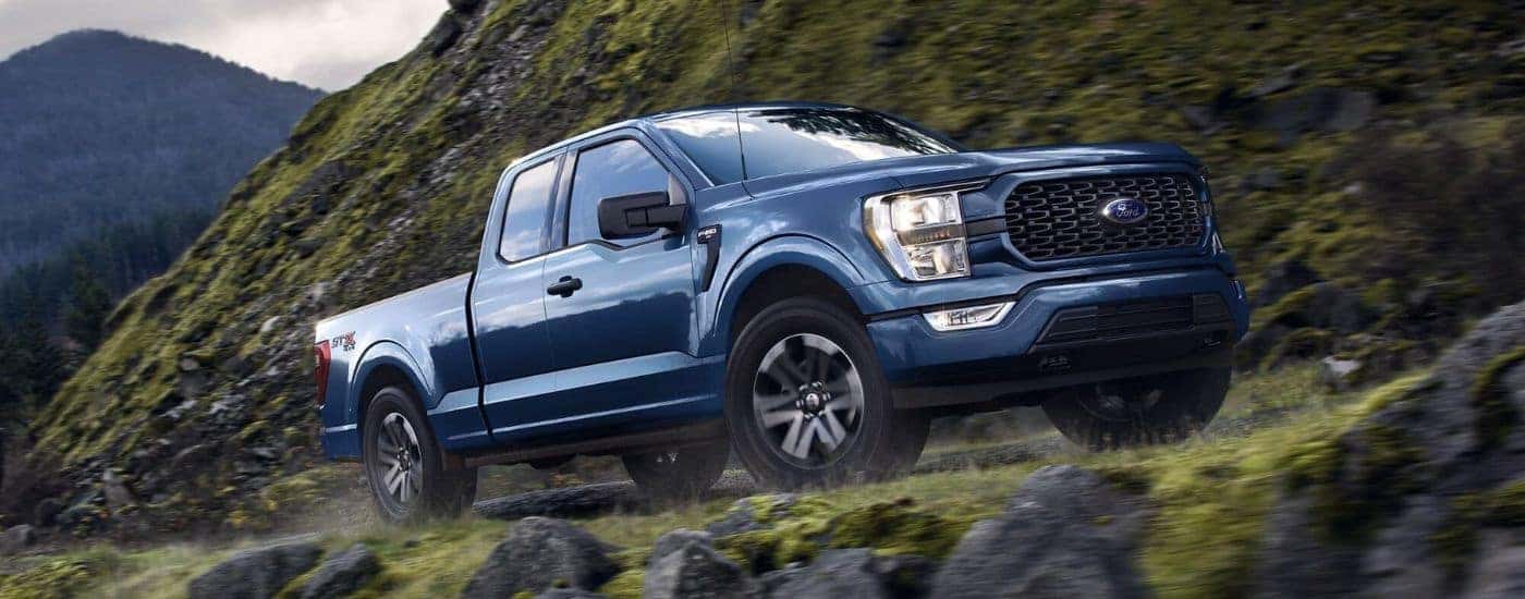 A blue 2023 Ford F-150 STX is shown driving on a mountain road after viewing a Ford F-150 for sale.