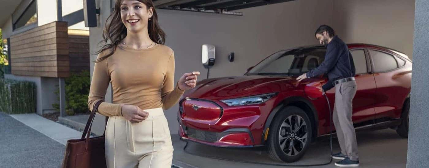 A red 2024 Ford Mustang Mach-E is shown charging in a garage near two people