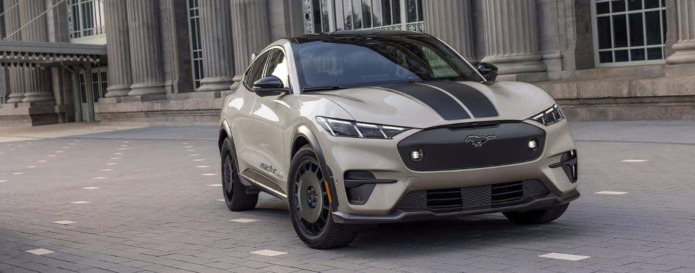 A tan 2025 Ford Mustang Mach-E Rally is shown parked near a city building.