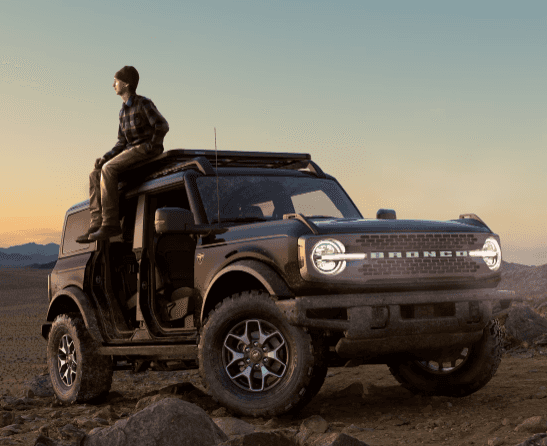 Man sitting on top of a Ford Bronco in a desert.