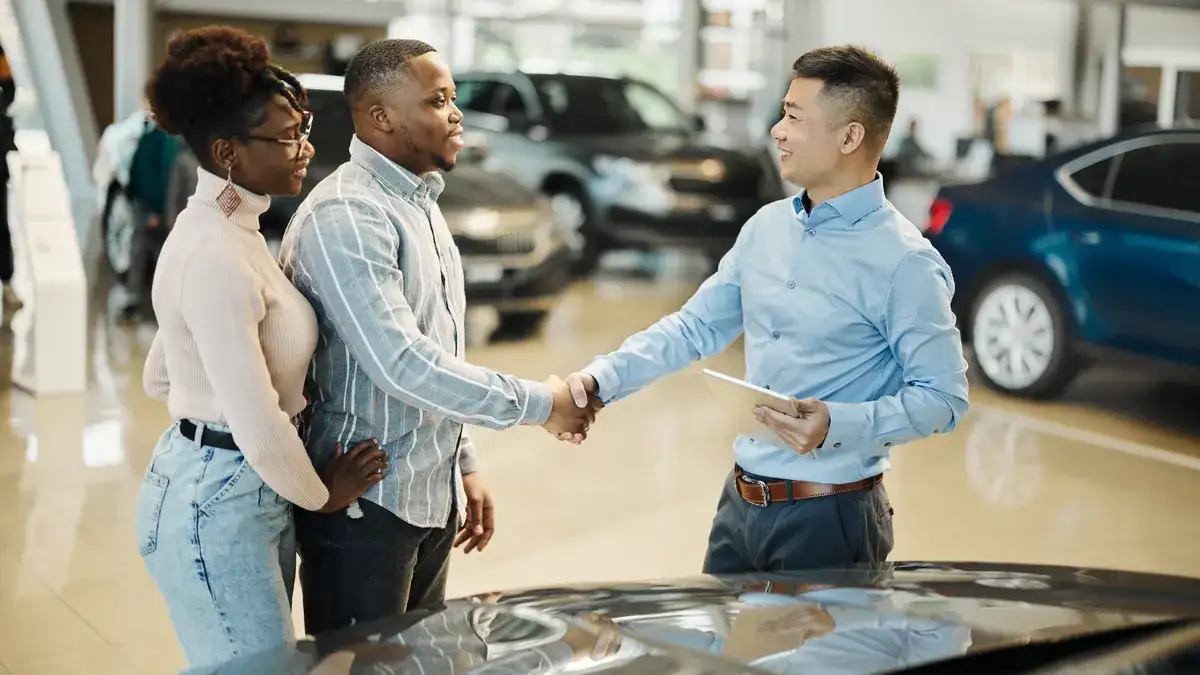 Couple shaking hands with a salesperson on the showroom floor at a family-owned Ford dealership in Harrisonville, Missouri