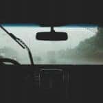 Rain coming down on the front windshield of a car while driving down the road.