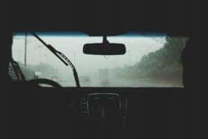Rain coming down on the front windshield of a car while driving down the road.