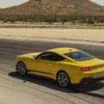 A Yellow Ford Mustang driving in the mountains on a paved road.
