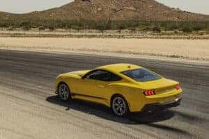 A Yellow Ford Mustang driving in the mountains on a paved road.