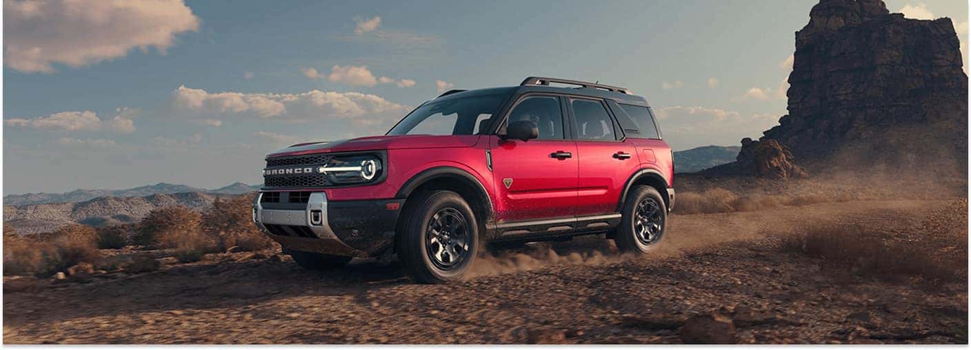 Red 2026 Ford Bronco Sport driving on a dirt off-road trail in a desert landscape.