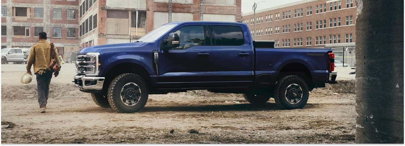 Side view of a blue 2026 Ford F-250 Tremor Super Duty pickup truck parked at a construction site.