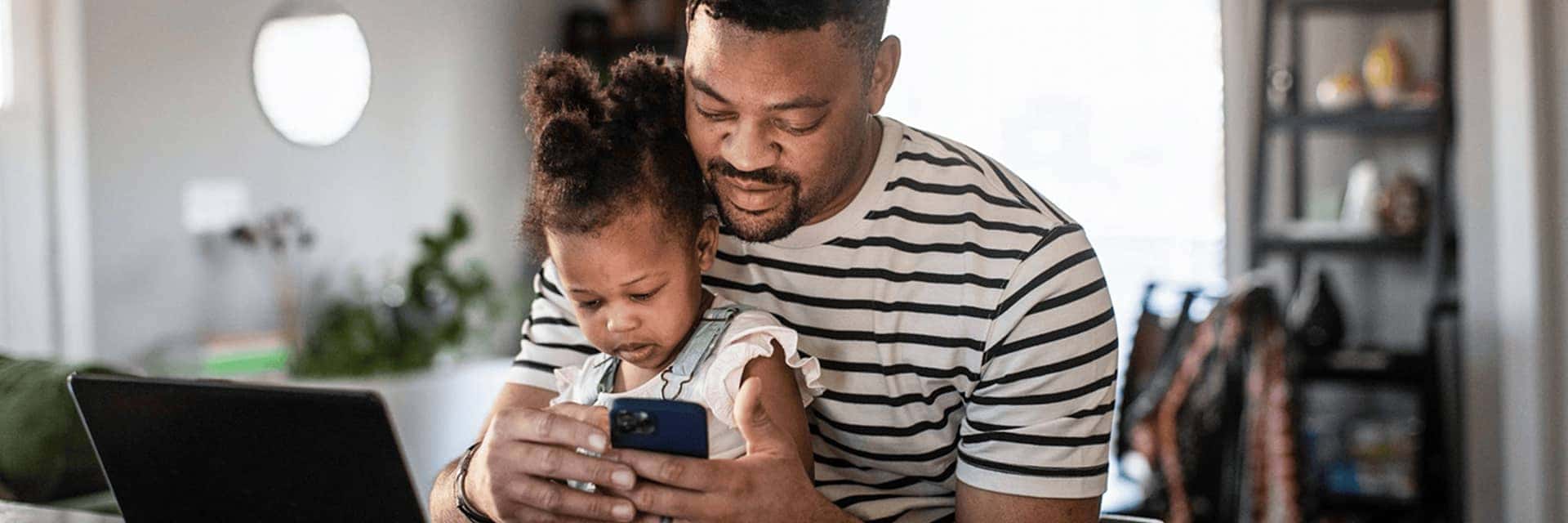 father looking at phone holding daughter