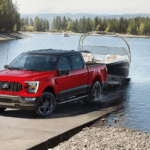 A red 2023 Ford F-150 XLT Heritage Edition is show towing a boat from a lake after visiting a Ford dealer near you.