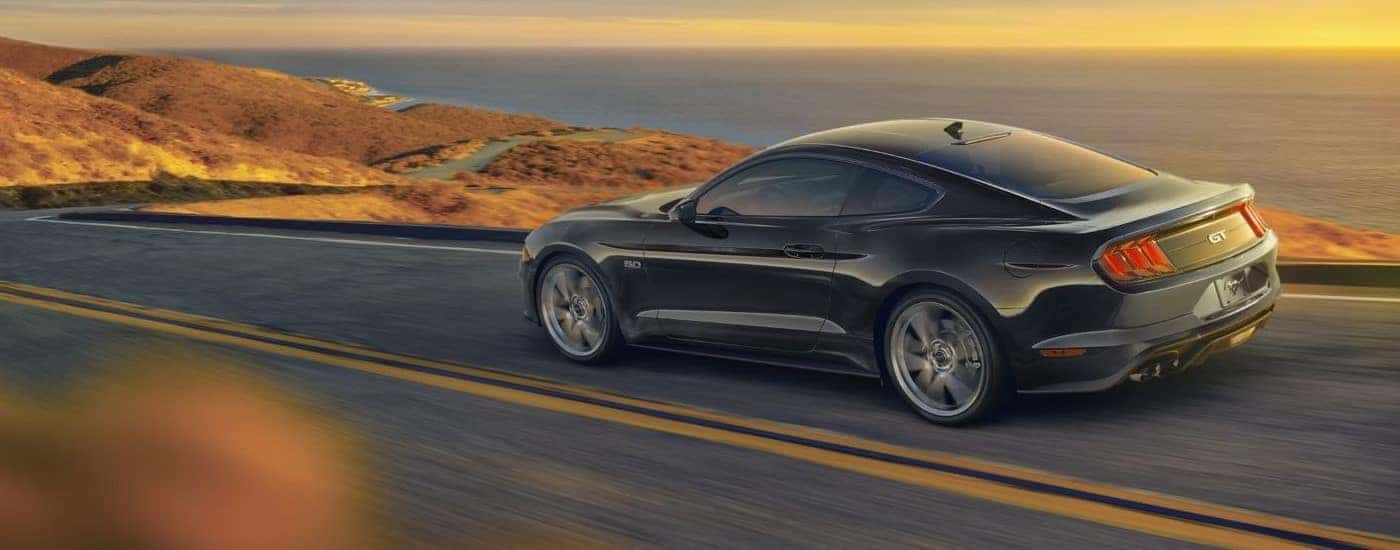 A black 2022 Ford Mustang GT is shown driving on a coastal road