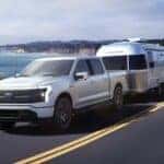 A white 2024 Ford F-150 Lightning is shown towing a trailer.