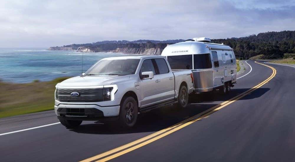 A white 2024 Ford F-150 Lightning is shown towing a trailer.