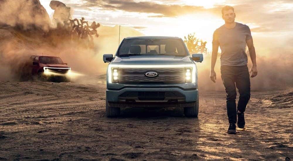 A blue 2024 Ford F-150 Lightning is shown from a front view while parked off-road.