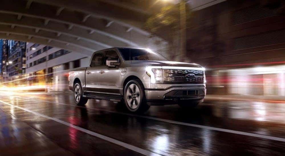 A silver 2024 Ford F-150 Lightning is shown driving from a dealer with a Ford F-150 Lightning for sale near Hayward.
