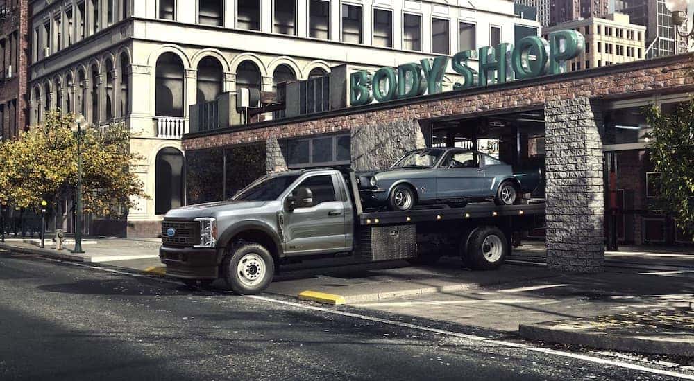 A grey 2023 Ford F-600 Chassis Cab is shown carrying a car out of a body shop.