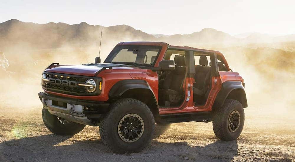 A red 2023 Ford Bronco Raptor parked off-road surrounded by dust.